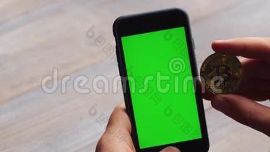 人使用垂直智能手机与绿色屏幕。 男子`手拿手机和一枚金币的特写镜头